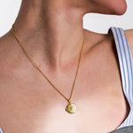 Gold sunburst locket necklace on woman wearing striped top, showcasing elegant jewelry fashion accessory.