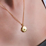 Gold pendant necklace with starburst design on skin, showcasing elegant jewelry fashion and style.