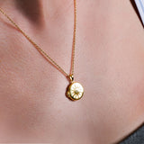 Gold pendant necklace with starburst design on skin, showcasing elegant jewelry fashion and style.
