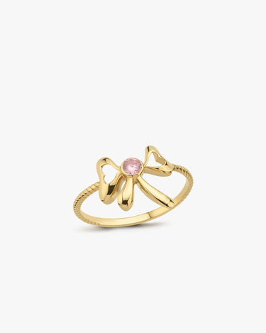 The Mionza Bow Ring in 14K Solid Gold showcases a delicate bow design adorned with a pink gemstone set at its center. The band's textured pattern enhances the overall elegance of this knot love ring, all highlighted against a plain white background to emphasize the intricate details.