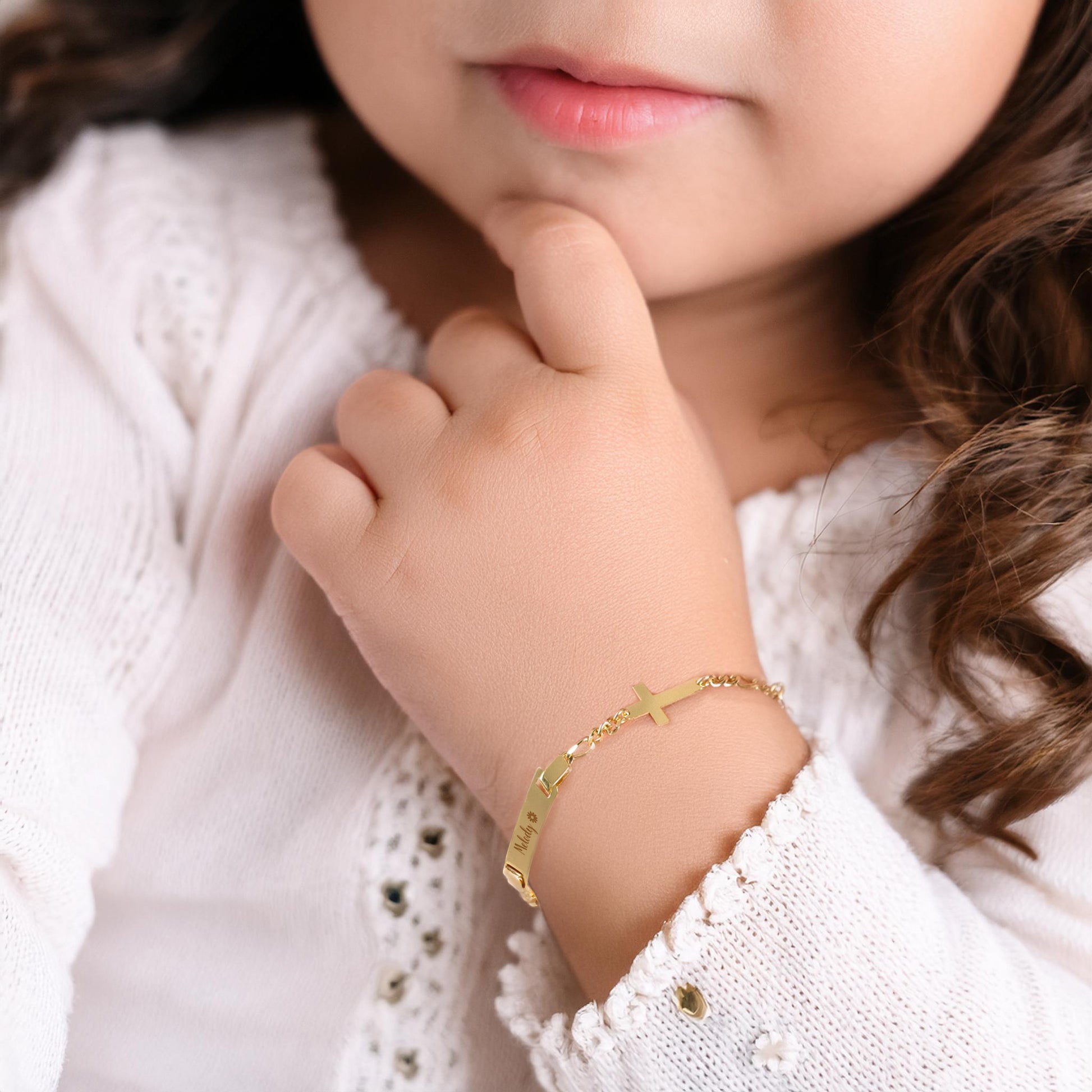 Close-up of a baby's hand wearing a gold baby bracelet with a cross bracelet.