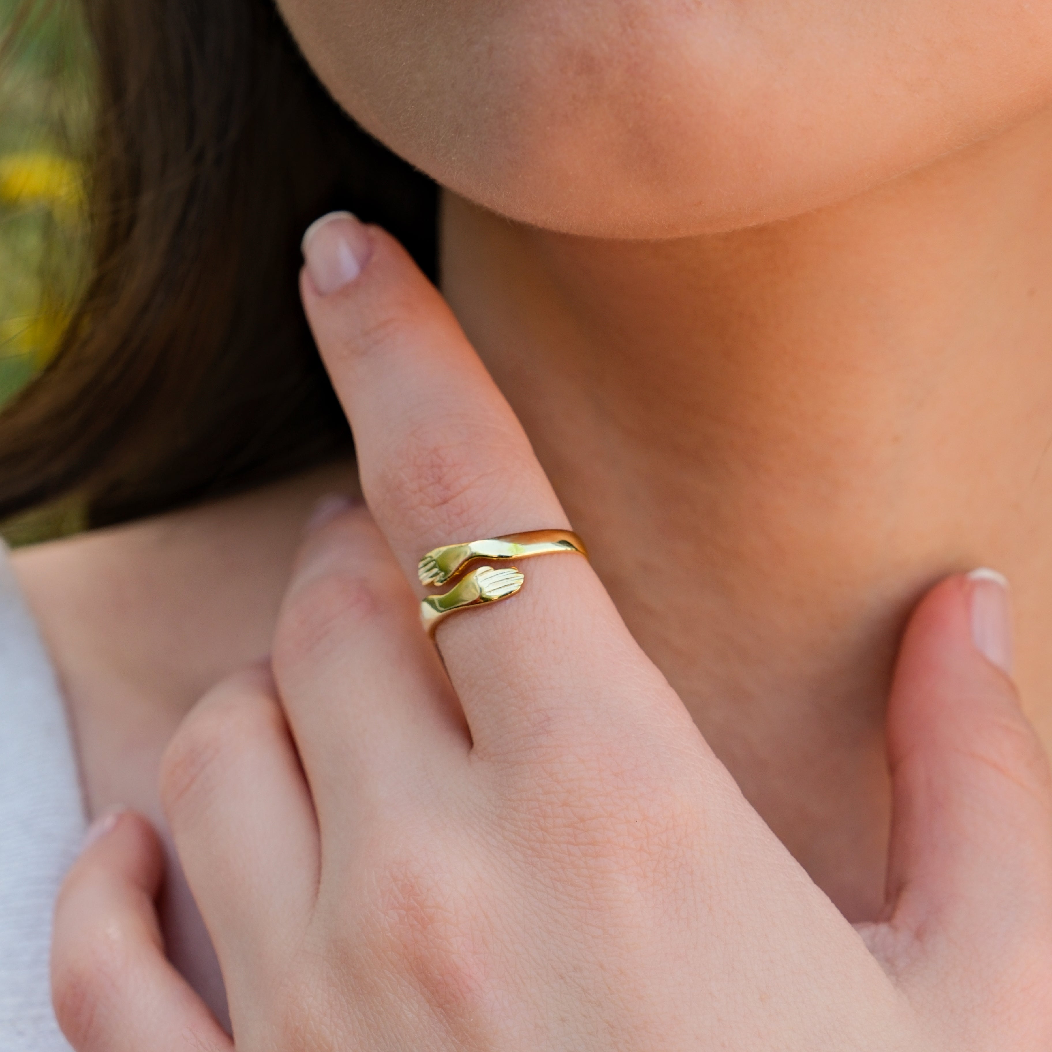 Close-up of a woman's hand wearing a unique gold ring with interlocking hands design.