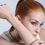 Woman with elegant gold cross bracelet posing thoughtfully, showcasing minimalist jewelry style against a neutral background.