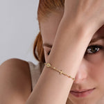 Woman wearing elegant gold cross bracelet, showcasing stylish jewelry fashion, with captivating gaze.