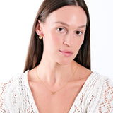 Woman wearing elegant gold jewelry with white knit top, highlighting necklace and earrings. Minimalist fashion style.