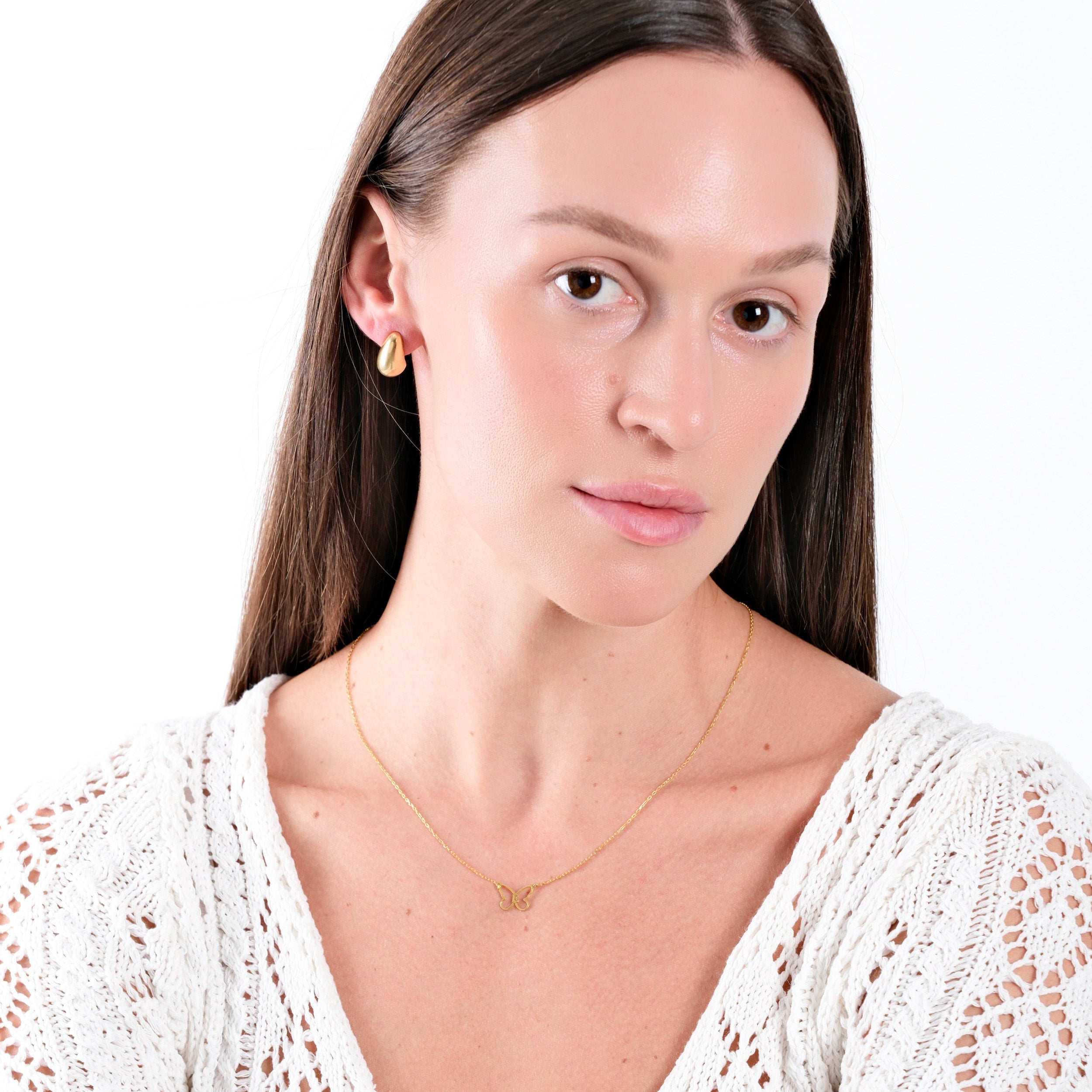 Woman wearing elegant gold jewelry with white knit top, highlighting necklace and earrings. Minimalist fashion style.