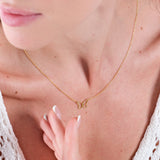 Close-up of woman wearing delicate gold butterfly necklace, white top, and elegant French manicure.