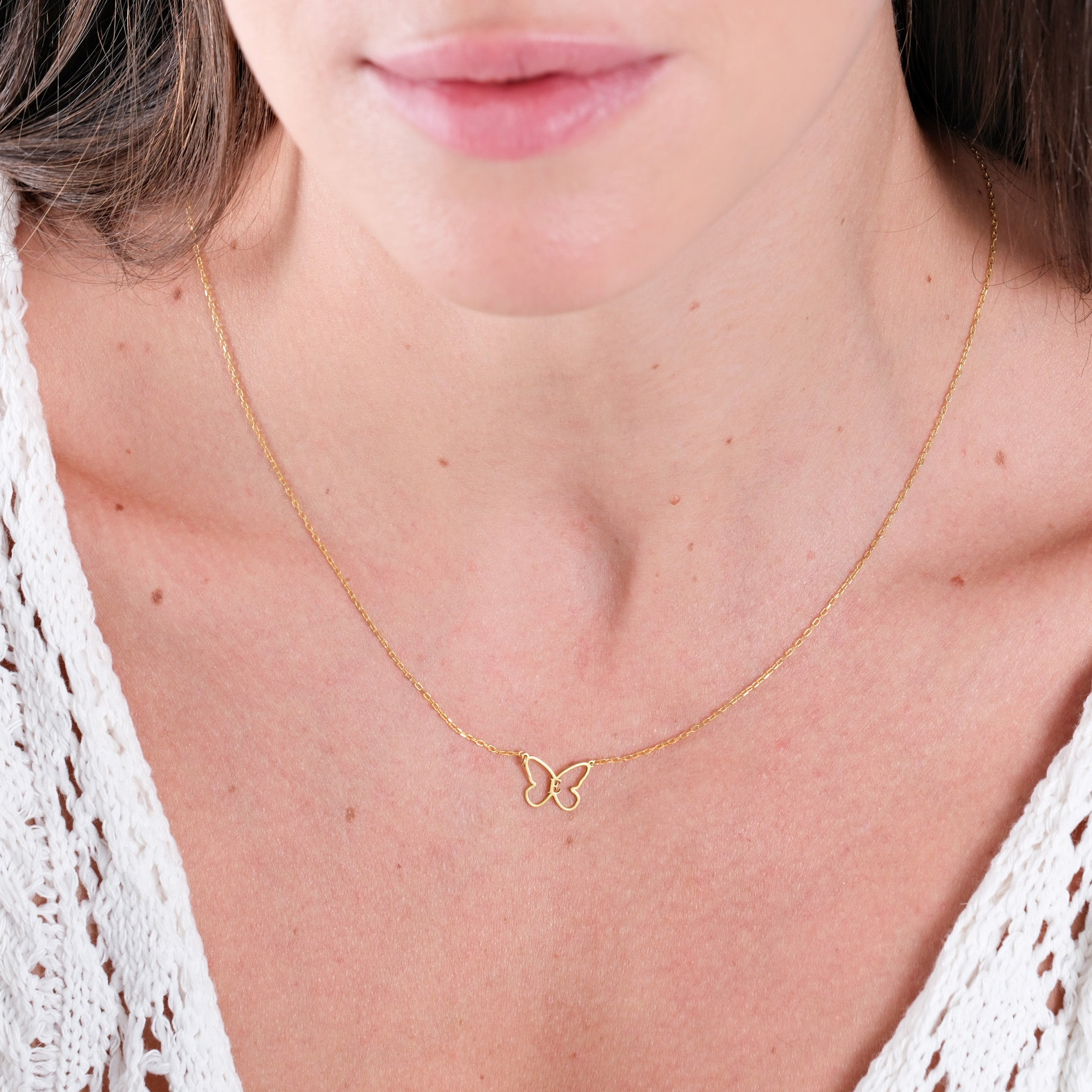 Woman wearing a delicate gold butterfly necklace with a white lace top, showcasing elegant jewelry style.