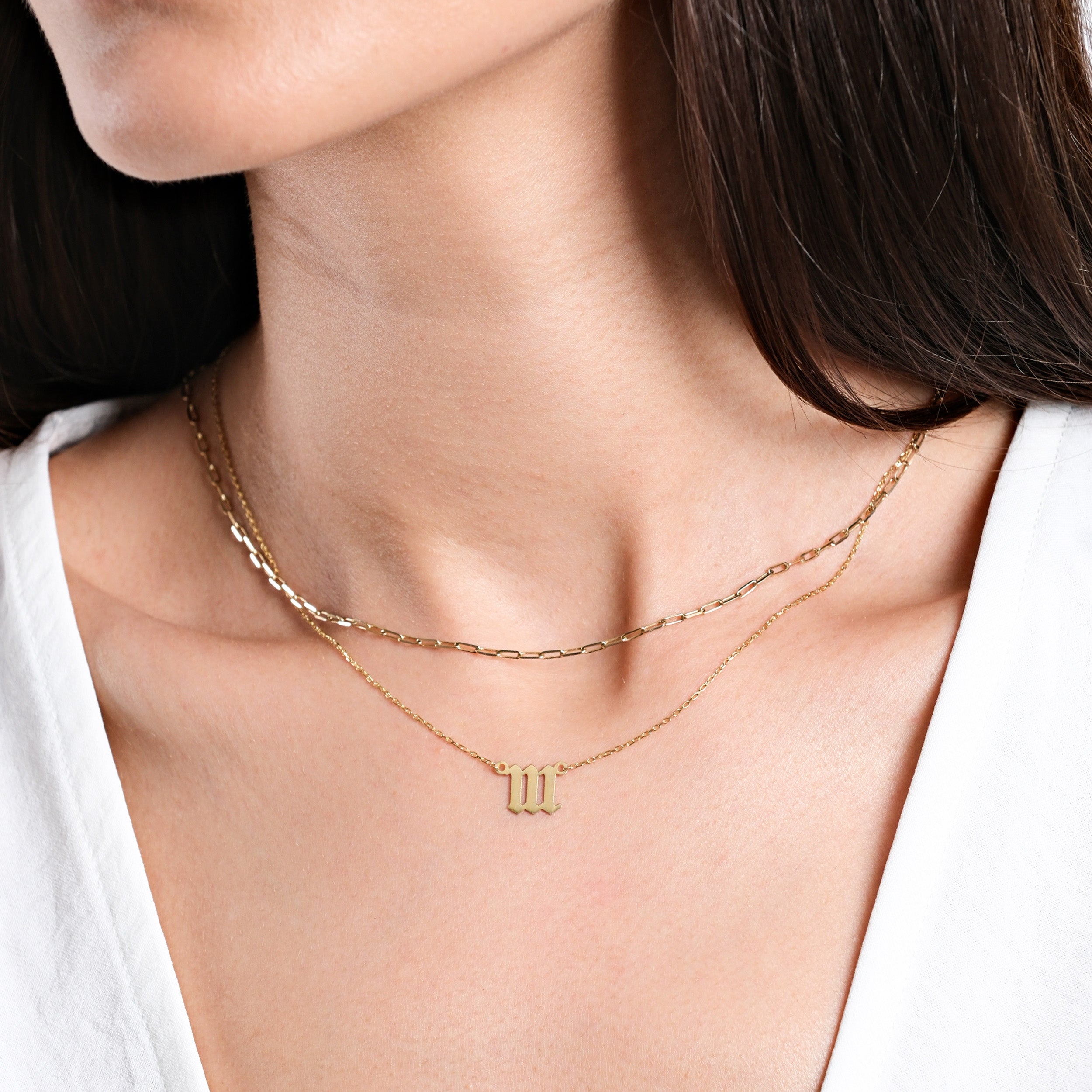 Woman wearing layered gold necklaces with a personalized initial pendant, close-up on neck and jewelry.