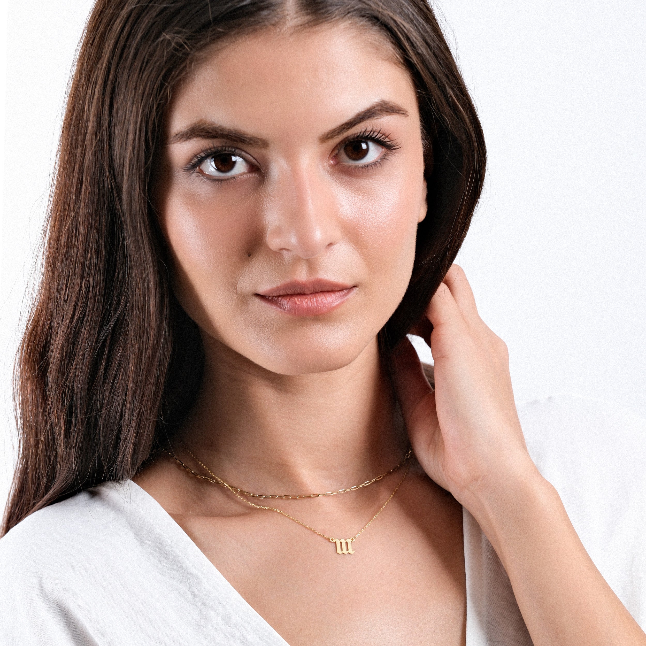 Woman wearing elegant gold necklace, showcasing minimalist jewelry style with white top and natural makeup.