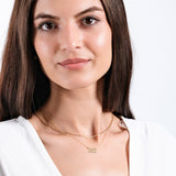 Woman with long brown hair wearing gold necklace and white shirt, showcasing elegant minimalist jewelry.