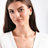 Woman wearing delicate gold necklace with number 222 pendant, white blouse, smiling gently, neutral background.