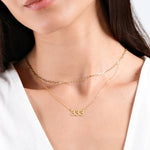 Woman wearing layered gold necklaces with "333" pendant, close-up on neck and white top.