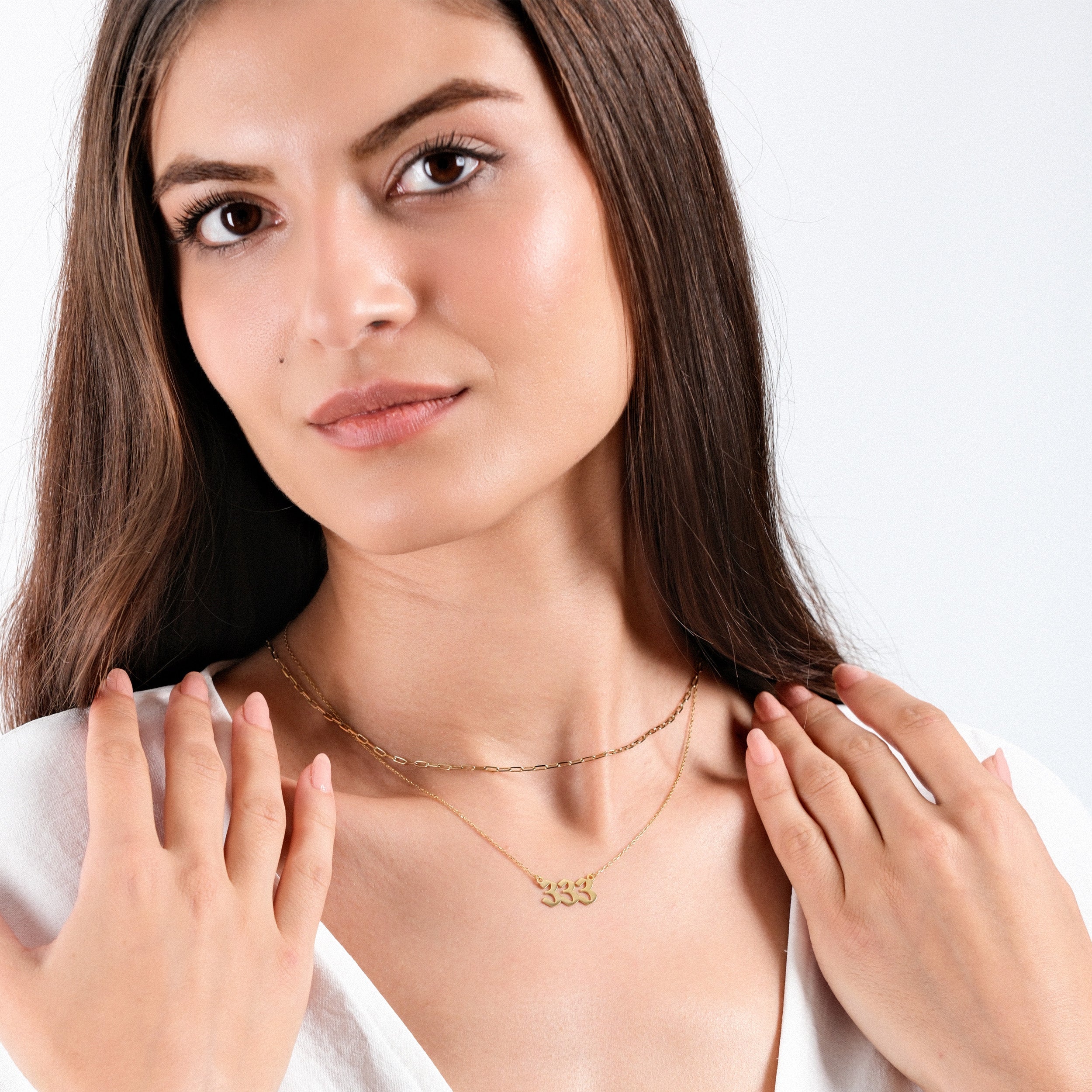 Woman wearing layered gold necklaces with "333" pendant, elegant fashion jewelry, close-up portrait.