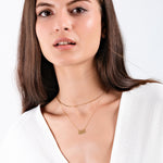 Woman wearing gold layered necklaces and white top, showcasing minimalist jewelry style.