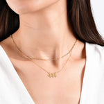 Woman wearing layered gold necklaces with angel number 444 pendant, close-up view against white background.