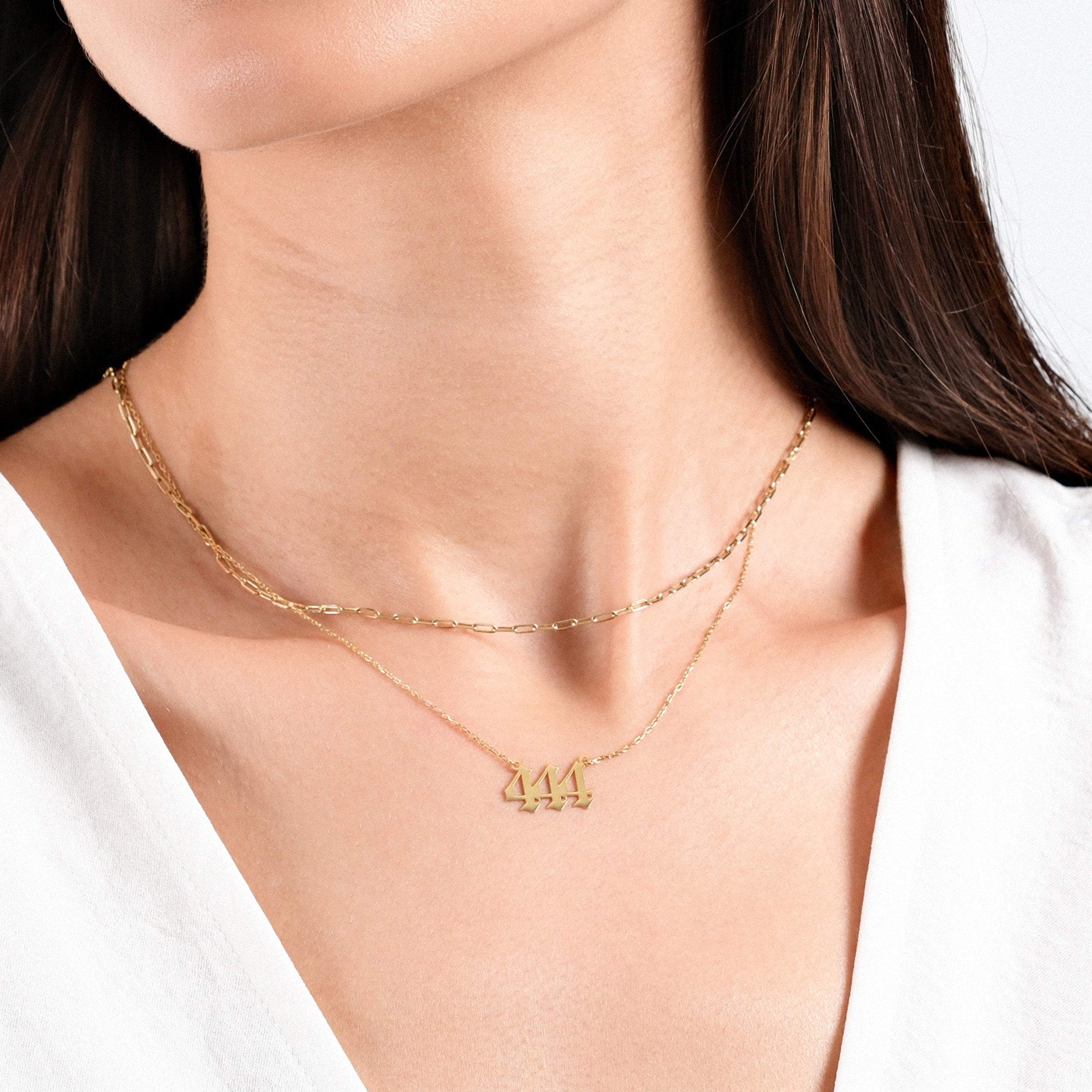 Woman wearing layered gold necklaces with angel number 444 pendant, close-up view against white background.