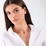 Young woman in white blouse wearing a gold necklace with "555" pendant, posing elegantly against a plain background.
