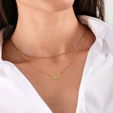 Woman wearing layered gold chain necklaces with number 555 pendant, white shirt background.