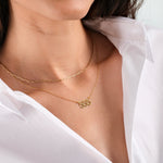 Woman wearing layered gold necklaces with a white shirt, featuring a pendant with the number "555".