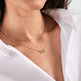 Woman wearing layered gold necklaces with a white shirt, featuring a pendant with the number "555".