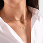 Woman wearing stylish gold necklaces with numbers, white shirt, elegant fashion accessory close-up.