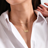 Woman wearing layered gold necklaces with a "666" pendant, styled with a crisp white shirt.