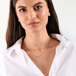 Woman with layered gold necklaces wearing a white shirt, showcasing elegant jewelry and minimalist style.
