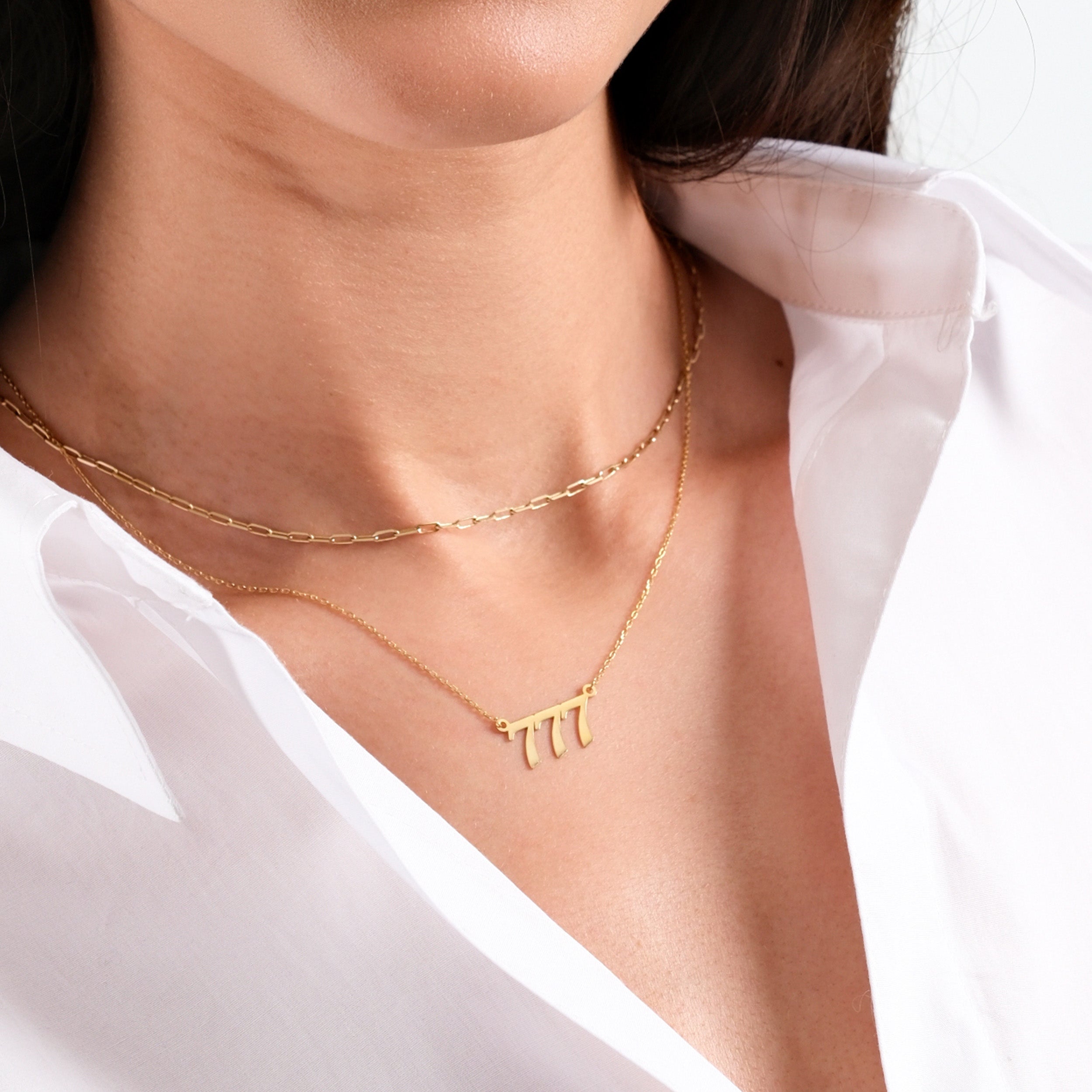Woman wearing elegant gold necklaces on white shirt, minimalist jewelry fashion.