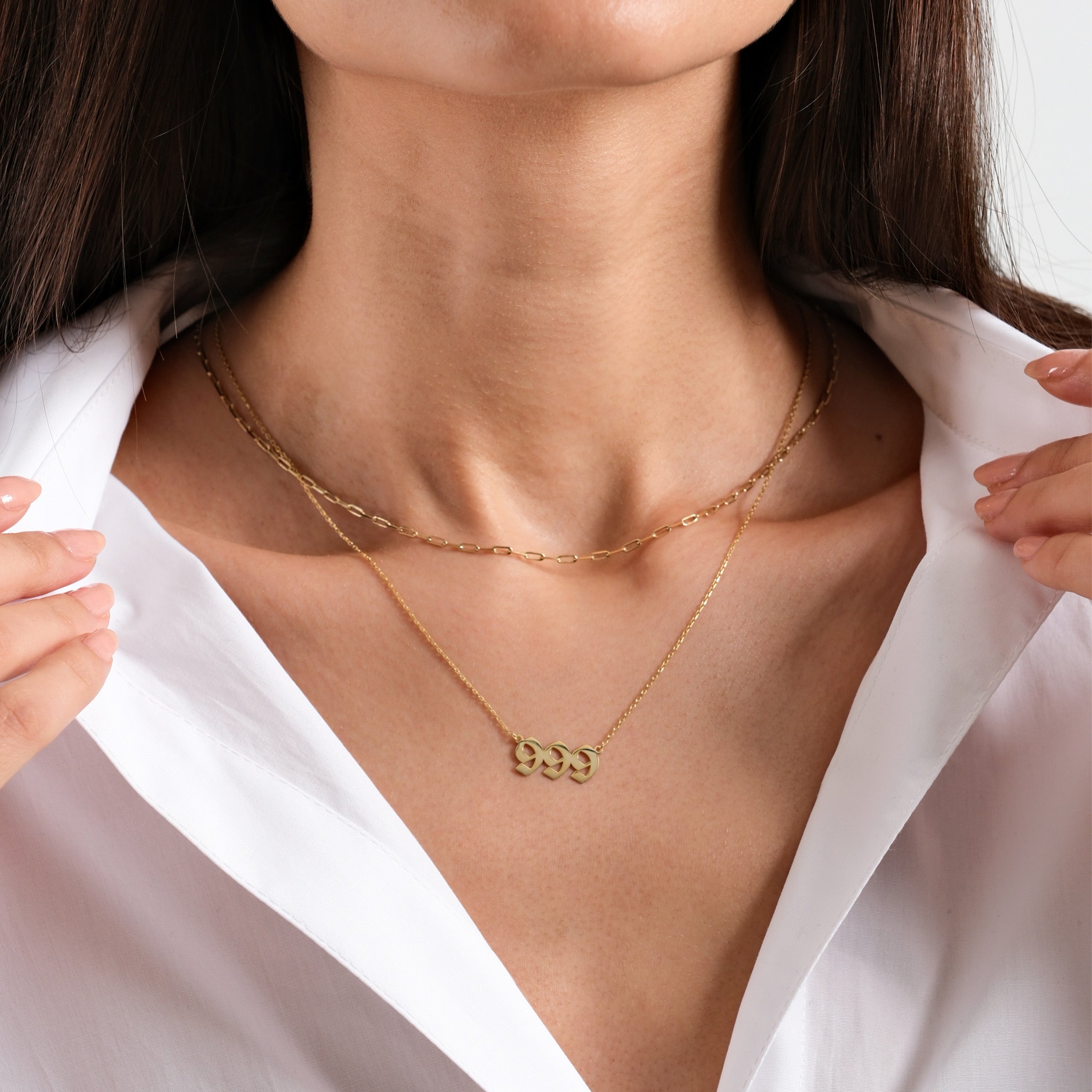 Woman wearing layered gold necklaces over white shirt, showcasing elegant jewelry style and fashion.