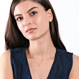 Woman wearing sleeveless denim top and gold necklace, posing against a white background with long, dark hair.