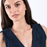 Woman wearing a denim dress and a delicate gold necklace with a simple pendant, expressing elegance and style.