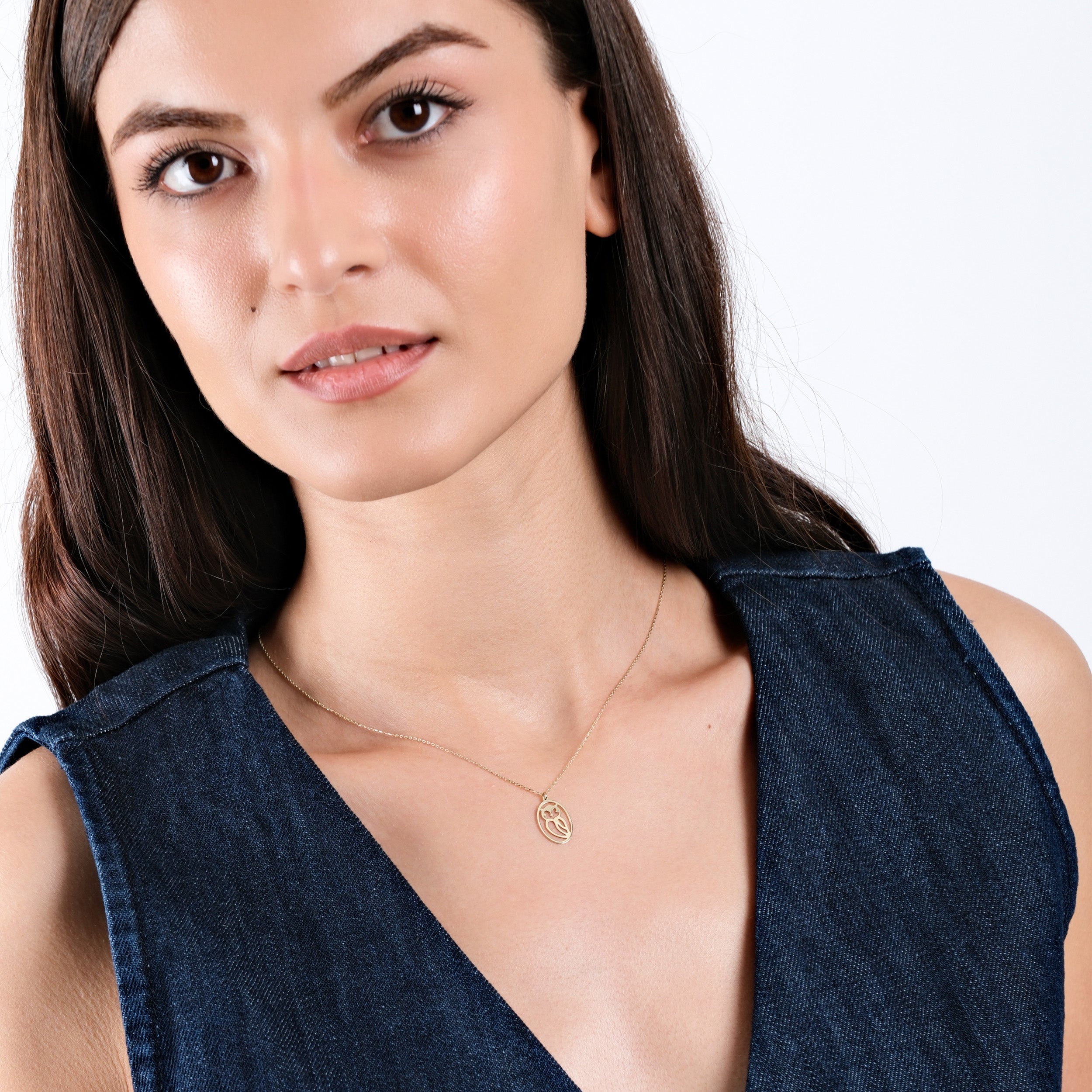 Woman wearing a denim dress and a delicate gold necklace with a simple pendant, expressing elegance and style.