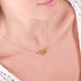 Gold name necklace on woman's neck, close-up, wearing white knitted top, personalized jewelry, elegant design.