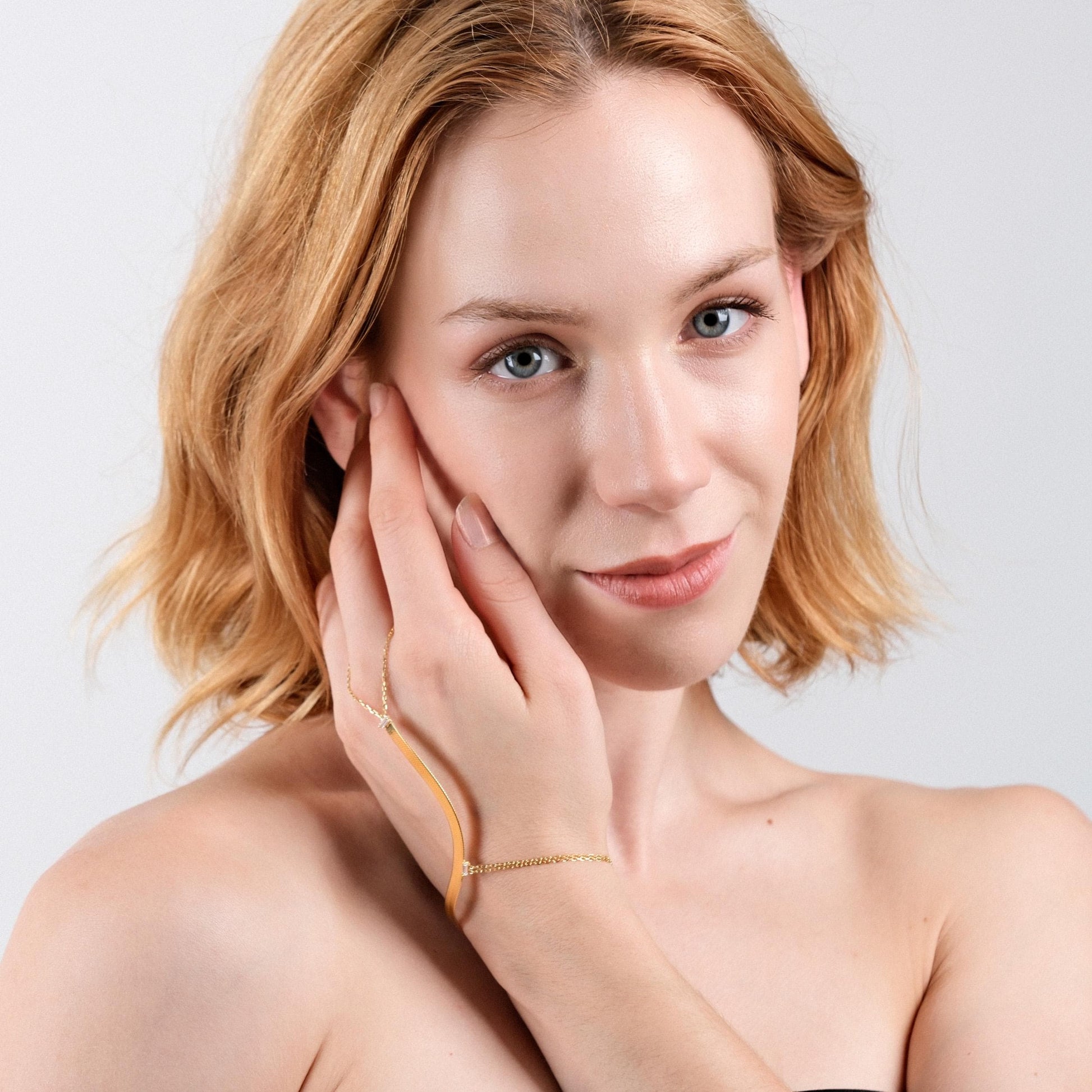 Portrait of a woman wearing an 18K gold herringbone hand chain bracelet, smiling softly.