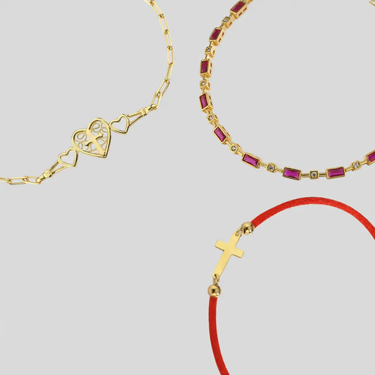 Gold bracelet with heart design and red gemstones on a light gray background
