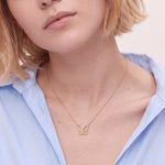 Close-up of a gold butterfly initial necklace worn with a light blue shirt, the open butterfly pendant with an initial at the collarbone