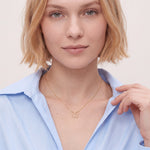 Woman wearing a dainty gold butterfly initial necklace on a fine cable chain with a light blue shirt