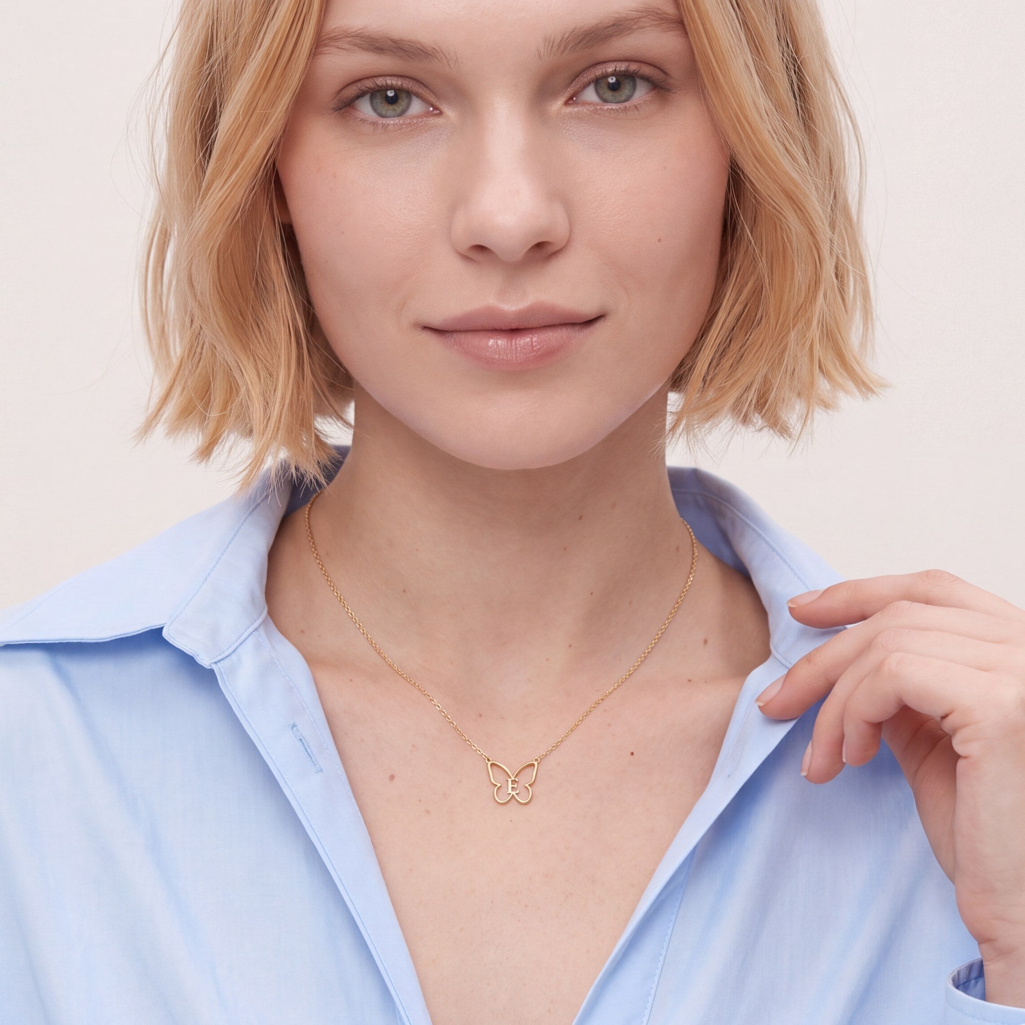 Woman wearing a dainty gold butterfly initial necklace on a fine cable chain with a light blue shirt