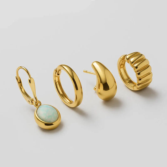 Set of gold hoop earrings and a gold earring with a gemstone on a light gray background