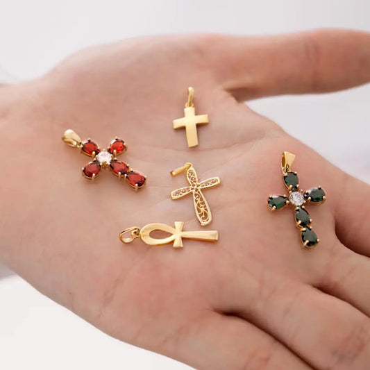 Gold cross pendants with gemstones on a hand