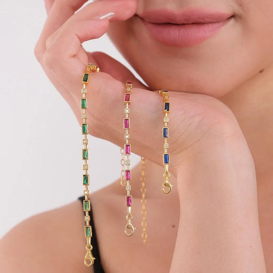 Three gold necklaces with gemstones held by a hand against a white background