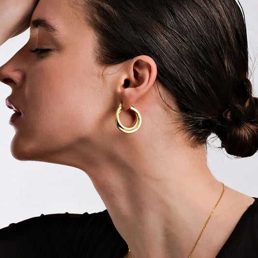 Close-up of a woman wearing gold hoop earrings with a neutral background