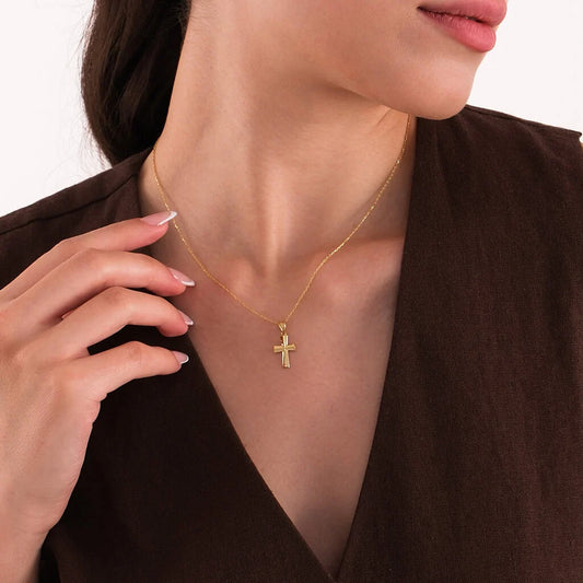 Gold cross necklace worn by a person against a neutral background
