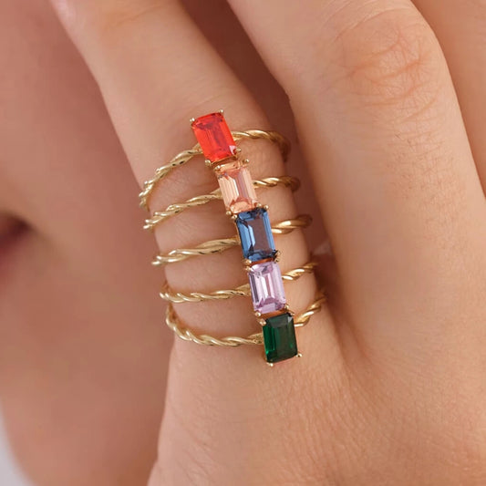 Stack of gold rings with colorful gemstones on a finger against a neutral background