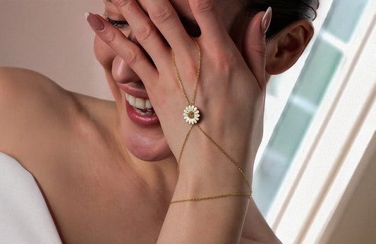 Woman wearing a delicate gold bracelet with a daisy design on her wrist.