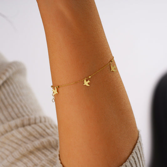 A gold dove bracelet elegantly wraps around a wrist against a soft-focus background.