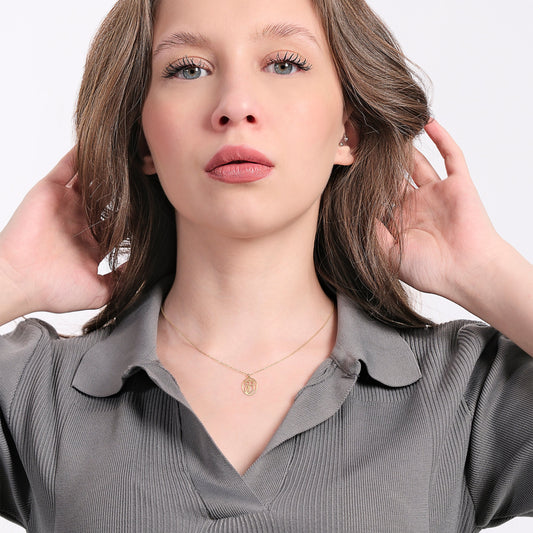 Portrait of a woman in a textured gray shirt with a gold owl necklace, looking directly at the camera.