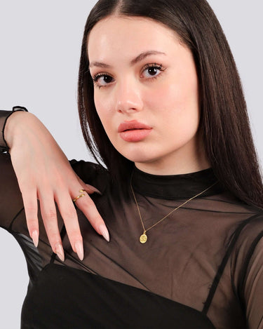 Portrait of a young woman in a sheer black top, gazing forward with a gold vermeil Om necklace visible against her skin.