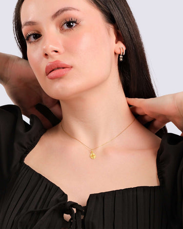 A model gracefully touches her hair, showcasing a 14K gold vermeil Eye of Horus necklace and matching earrings.